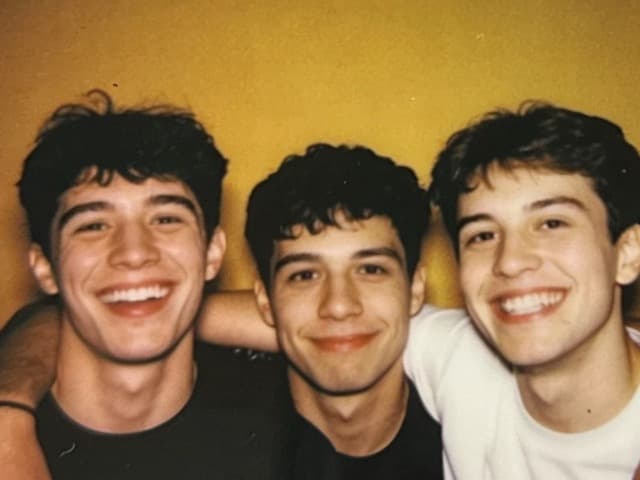 The same three friends grinning against a mustard wall