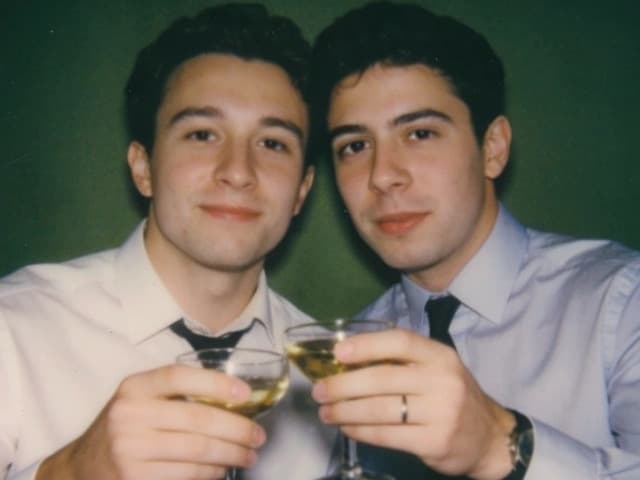 The same two friends, glasses lowered, laughing